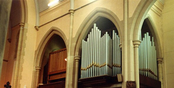 Pipe organ inside a church with arched stone architecture.