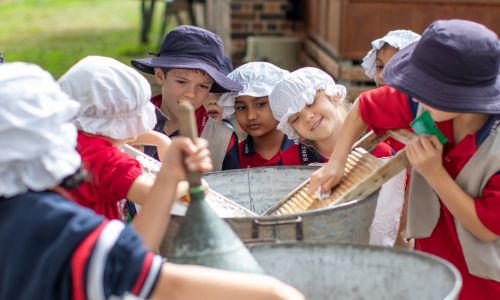 Children wearing period costumes wash clothes using washboards.