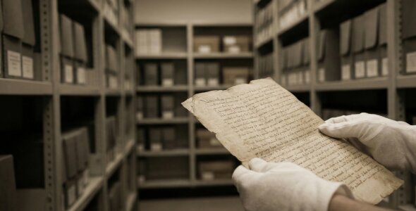 Person wearing gloves holding an old manuscript in an archive.