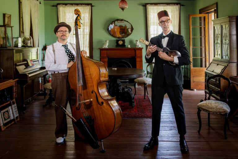 Two musicians with vintage instruments in a period-style room.