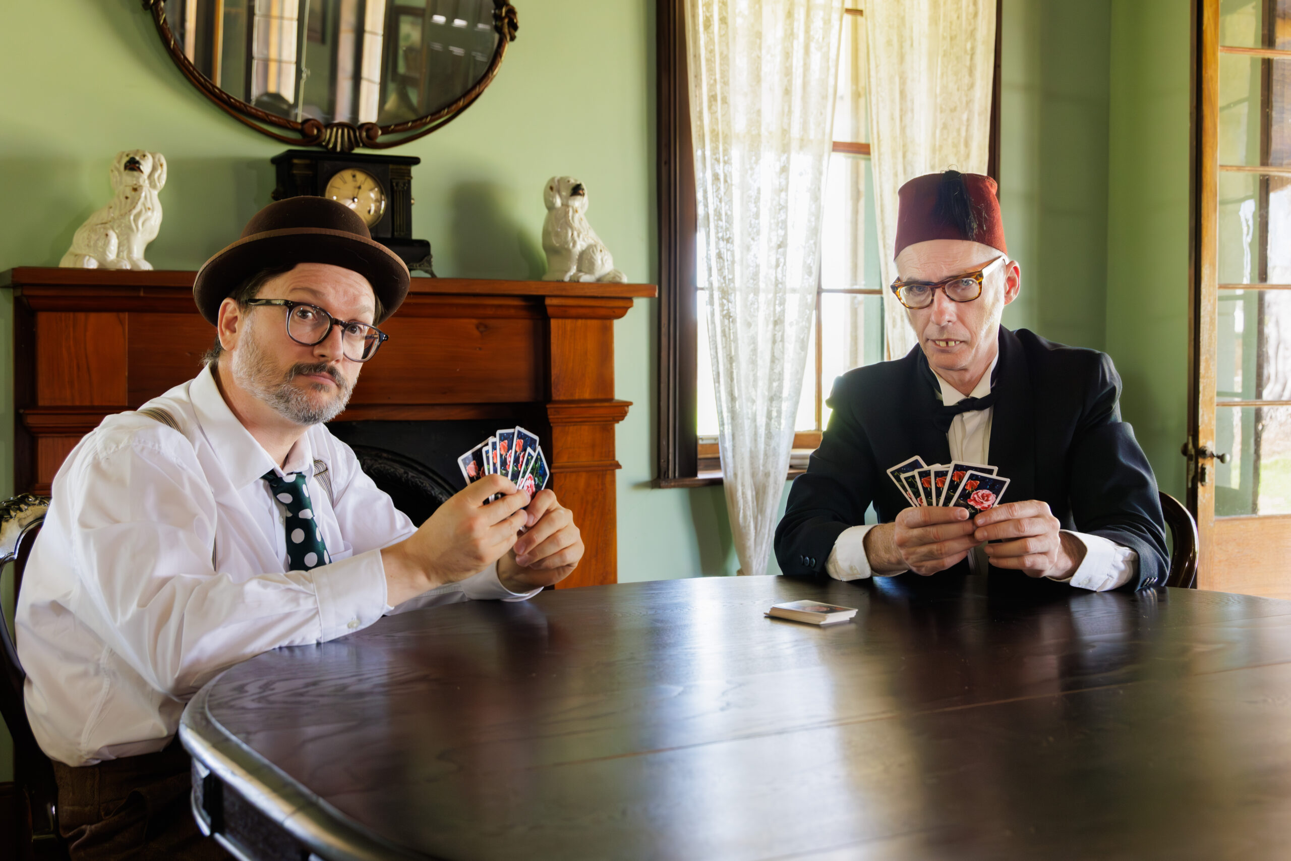 Two men playing cards at a wooden table in a vintage room.