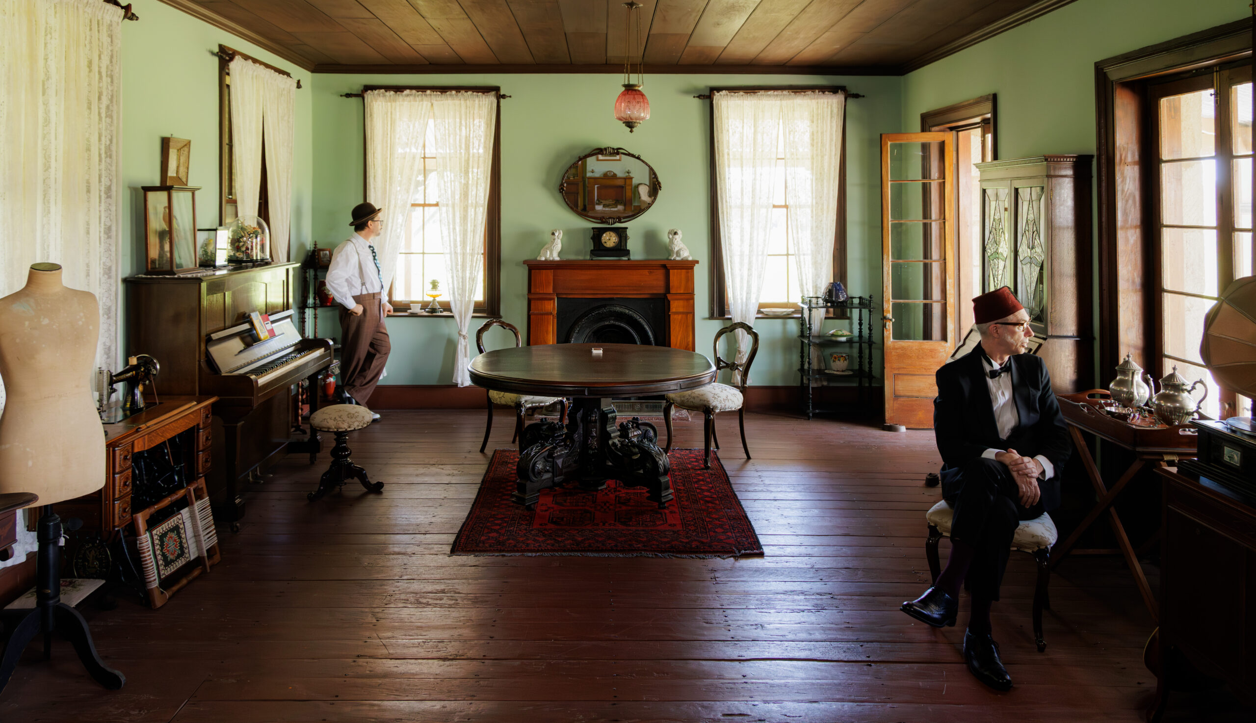 Two men in a vintage living room with period furnishings.