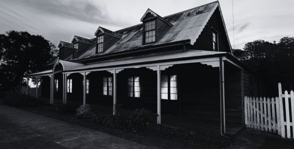 Black and white image of an old house with a porch at dusk.